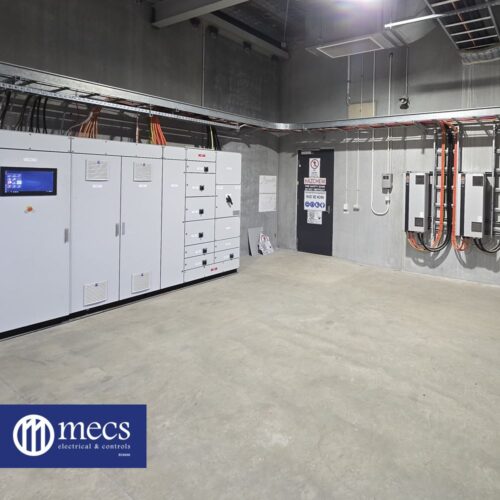 A large room filled with electrical equipment, with prominent electrical control panel and numerous wires
