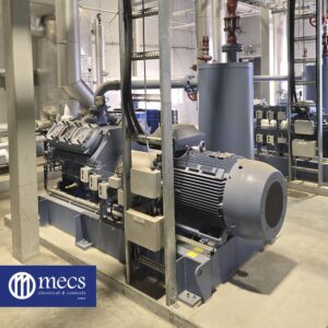 Industrial air compressor connected to HVAC control system, positioned among pipes, gauges, and other industrial equipment