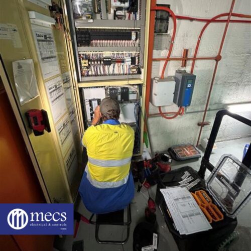 Electrical mechanic in a yellow vest servicing an electrical control panel at Westralia Square Car Park during maintenance work
