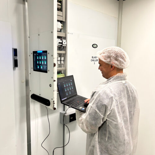 A man in a white coat operates a laptop, managing an HVAC control system at Fiona Stanley Hospital’s Main Kitchen