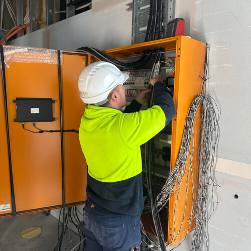 Technician in green vest and hard hat from an industrial electrical company in Perth installing switchboard at Ocean Reef Marina