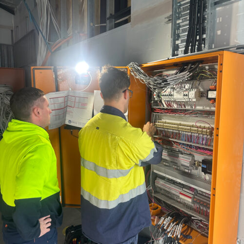 Two technicians in a green vest from an industrial electrical company in Perth commission a mechanical switchboard at Ocean Reef Marina