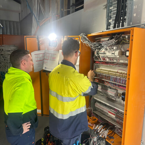 Two technicians in a green vest from an industrial electrical company in Perth commission a mechanical switchboard at Ocean Reef Marina