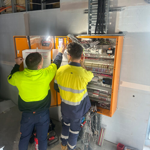 Two technicians in a green vest from an industrial electrical company in Perth commission a mechanical switchboard at Ocean Reef Marina