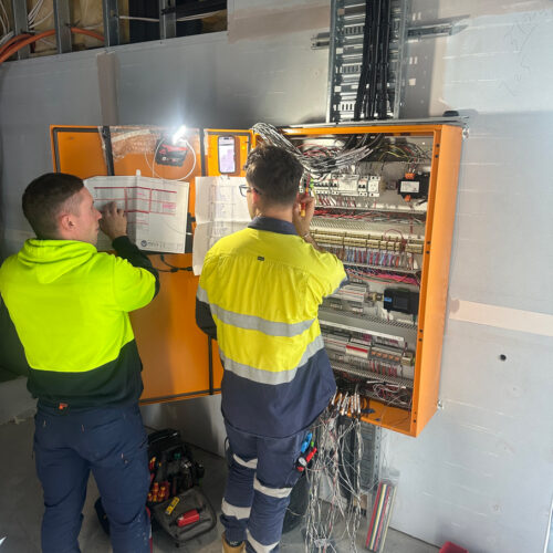 Two technicians in a green vest from an industrial electrical company in Perth commission a mechanical switchboard at Ocean Reef Marina