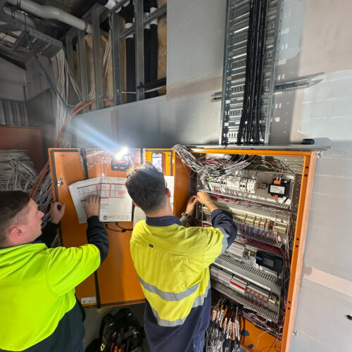 Two technicians in a green vest from an industrial electrical company in Perth commission a mechanical switchboard at Ocean Reef Marina