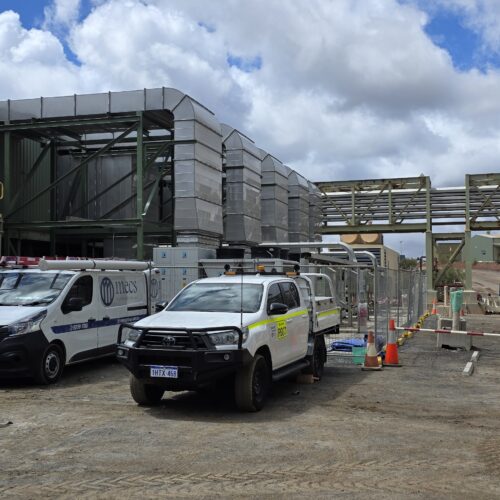 Two service trucks parked outside Boddington Gold Mine building during HVAC control system installation and site operations