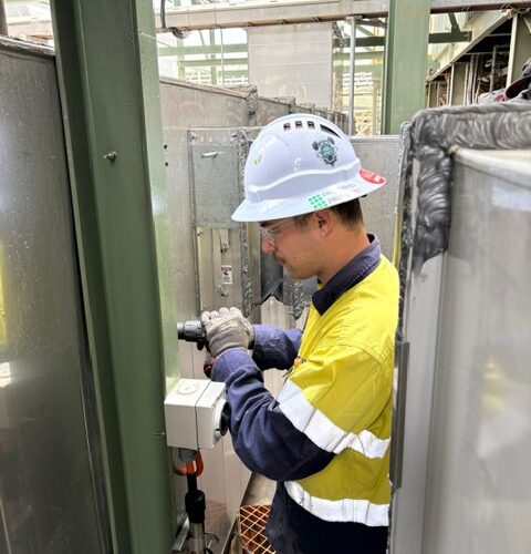 An electrical mechanic in a hard hat and safety vest adjusts an HVAC control system machine at Boddington Gold Mine