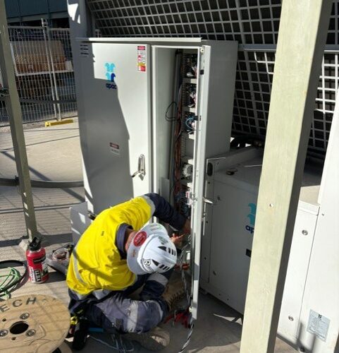 Technician repairing large air conditioning unit, adjusting HVAC control system components for optimal performance