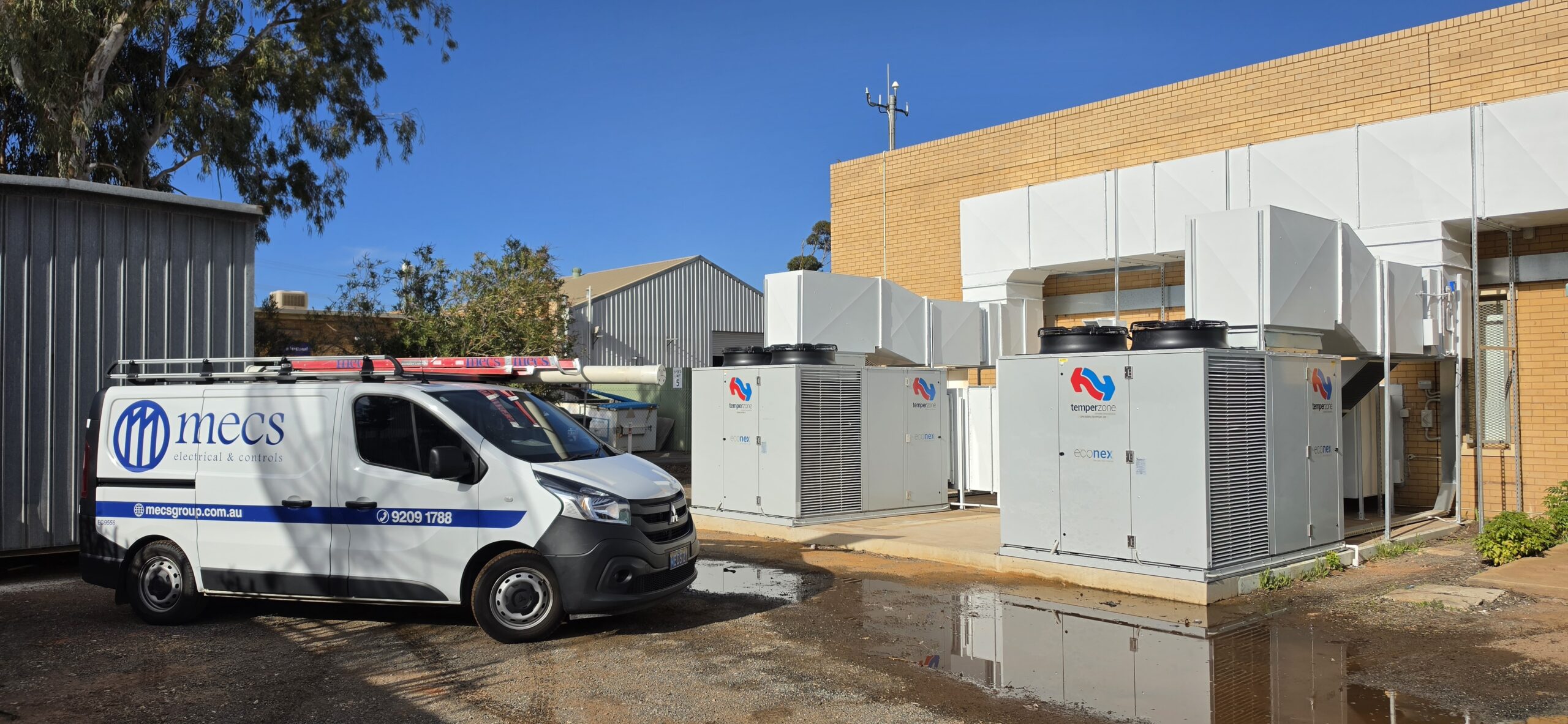 MECS Electrical & Control service van parked beside large commercial outdoor HVAC control system units outside a building.